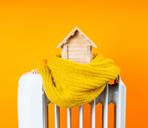 Maison posée sur un radiateur avec une écharpe jaune enroulée autour, symbolisant la chaleur et le confort du chauffage